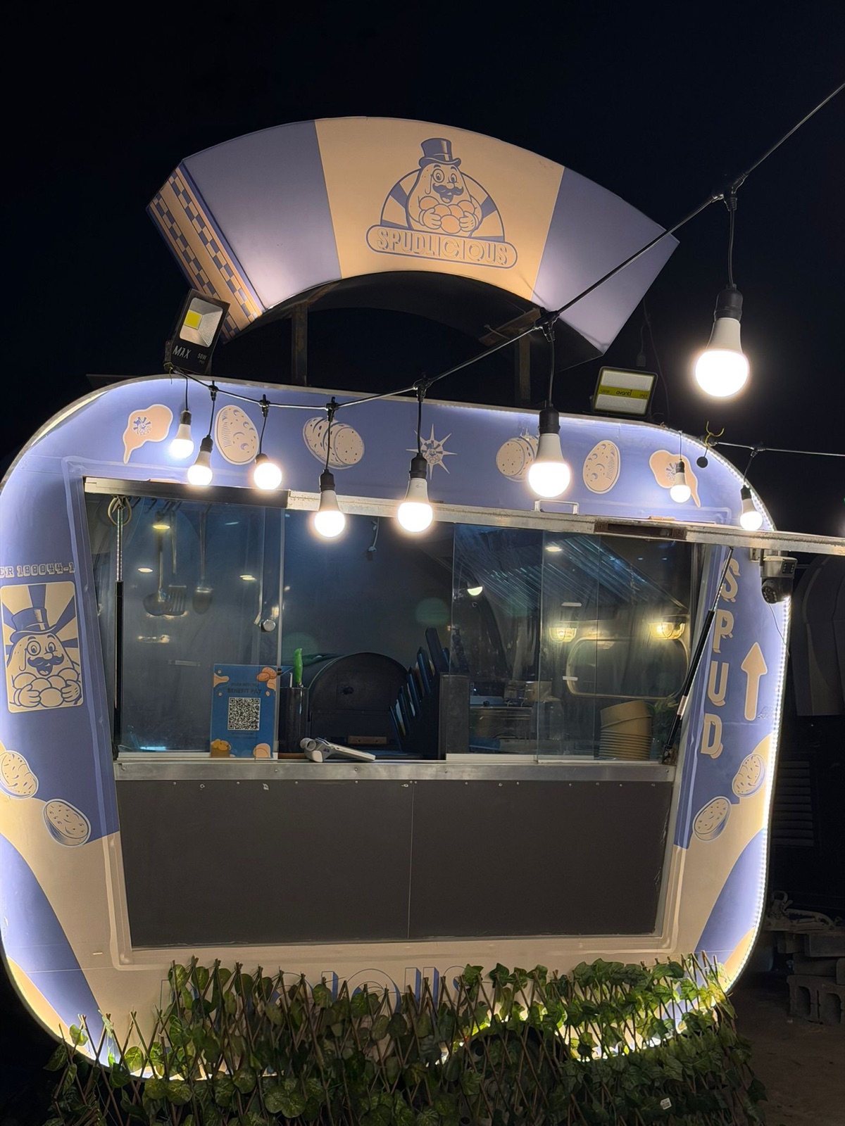 The Spudlicious truck front glowing under string lights, awning lit with the Mr. Spud logo